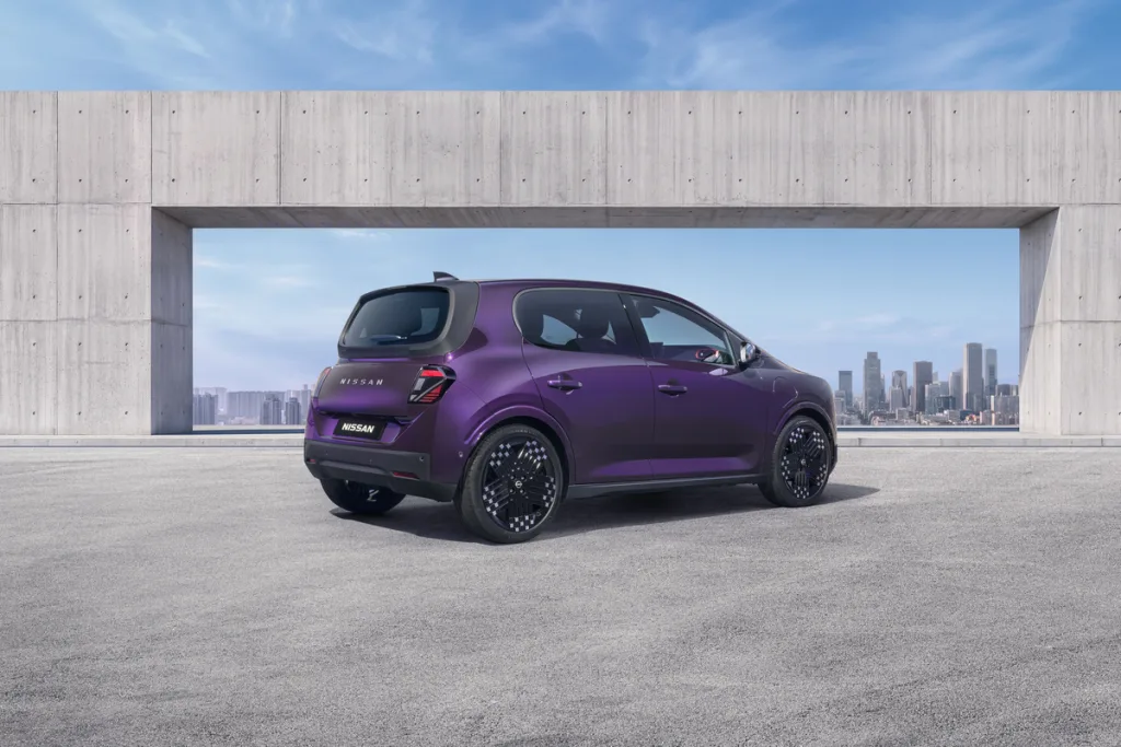 Three-quarter rear view of a purple Nissan PIXO electric city car parked beneath a modern concrete structure, with a city skyline in the background.